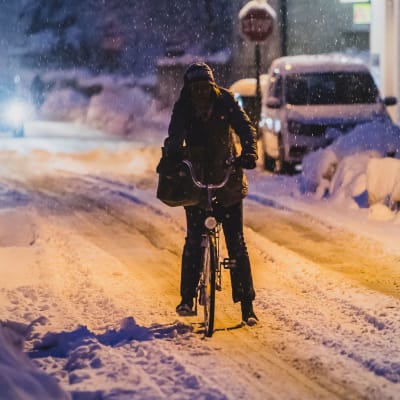 En person cyklar i snöigt väder en kväll.