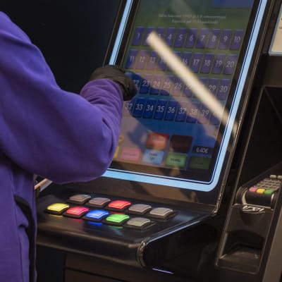 Ihmisen sormi koskettaa peliautomaatin näyttöä, lähikuva. 