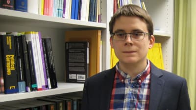 fredrik malmberg står med kavaj vid en bokhylla med statsvetenskaplig litteratur