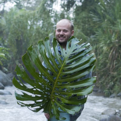 Carl Lingren med ett stort palmblad står med en flod bakom sig