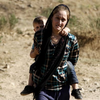 Yazidisk kvinna flyr undan IS med sin son på ryggen.