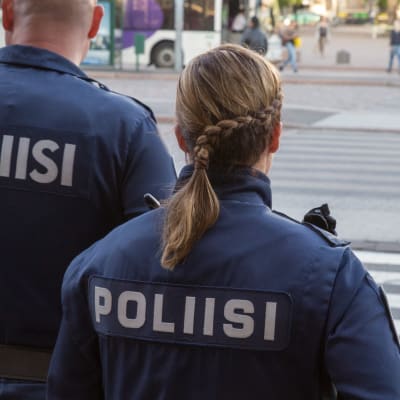 Två uniformklädda poliser står med ryggen mot kameran och blickar ut över Järnvägstorget i Helsingfors.