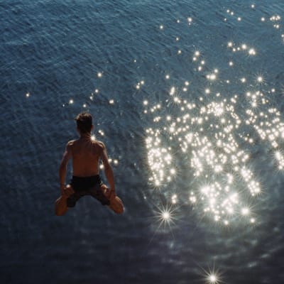Ung kille hoppar ner i solglittrande hav.