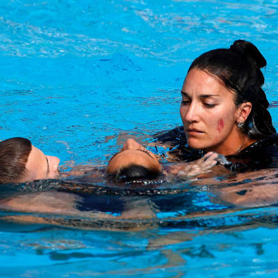 Anita Alvarez hjälps från bassängen av tränaren Andrea Fuentes och en badvakt.