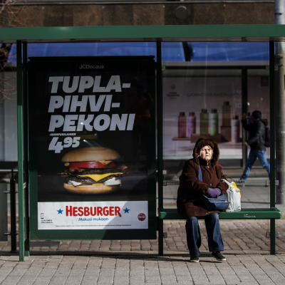 En äldre person sitter vid en spårvagnshållplats i Helsingfors centrum.
