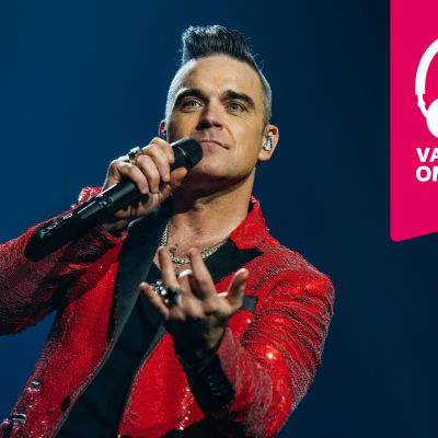 Robbie Williams sjunger i en mikrofon som han håller i handen.