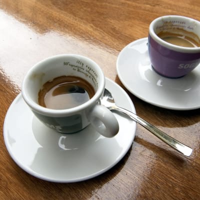 Kaksi espressokuppia kiiltävällä puisella pöydällä.