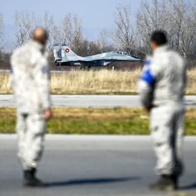 Ett jaktplan av typen MiG-29 landar. I förgrunden står två piloter.