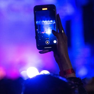 Närbild av en persons hand som filmar med en Iphone på en konsert.