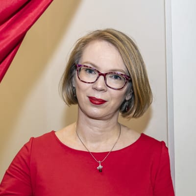 Maria Turtschaninoff tittar fram bakom en röd gardin i ett rum intill bokmässans utställningsutrymmen. 
