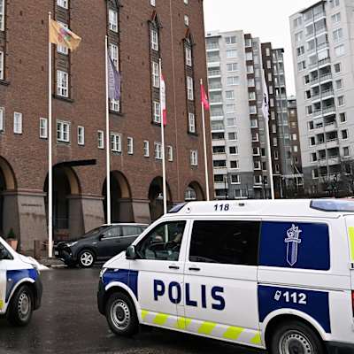Två polisbilar parkerade utanför ett stort brunt tegelhus inne i en stad. 