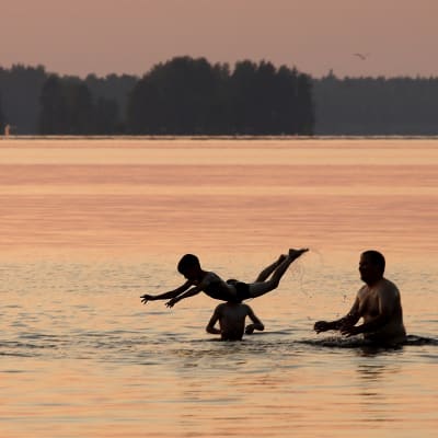 Aikuisia ja lapsia uimassa auringonlaskun aikaan.