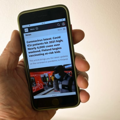 Hand holding a smartphone which is displaying the Yle News website.