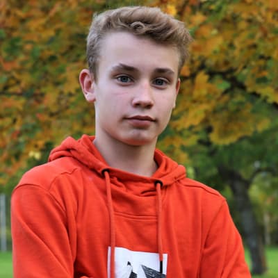 Oliver "Ollie" Takanen tittar in i kameran, har händerna i kors. Höstlöv i bakgrunden.