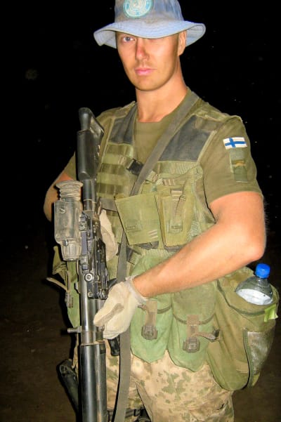 Man i militärutrustning står med ett gevär i händerna.