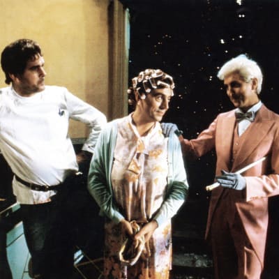 Scen ur Monty Python The Meaning of Life. Terry Jones i mitten med papiljotter i håret. John Cleese till vänster och Eric Idle till höger.