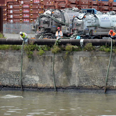 Työntekijät koettavat imeä öljyä pois Polcevera-joesta Genovassa 23.4. 2016.