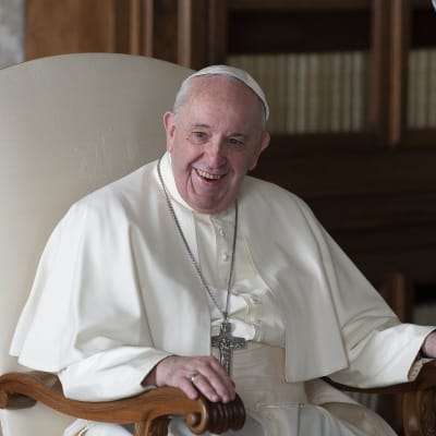 Påven Franciskus sitter på en stol och skrattar 