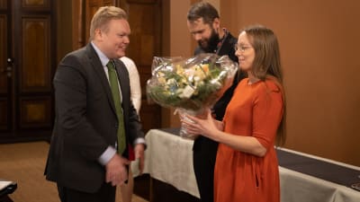 Kristiina Tiainen tar emot blombukett av forsknings- och kulturminister Antti Kurvinen, Sagalunds museichef John Björkman i bakgrunden.