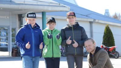 Adam Nässlin, Nico Källberg och Hugo Sundsten ger tummen upp för Skolmusik 2017. Läraren Tobias Tåg sitter på huk bredbid pojkarna.