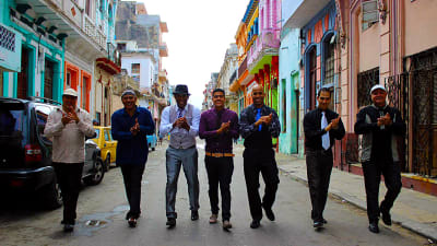 Sju män går i bredd på en gata i Havanna.