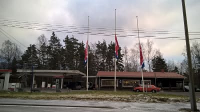 En bränslemack och tillhörande kafébyggnad, Teboil-flaggor i halvstång.