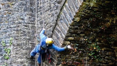 En man hänger från ett rep och arbetar med att ta loss växter från ett slottsvalv på Dunans castle. 
