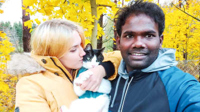 En kvinna med en katt i famnen poserar tillsammans med en leende man. Bakom dem syns gula höstlöv.