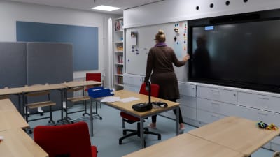 Bild av lärare som drar undan en skrivtavla framför en skärm i ett klassrum. 