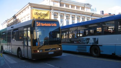 Två stadsbussar vid Salutorget i Åbo. I bakgrunden finns Åbo Svenska Teater.