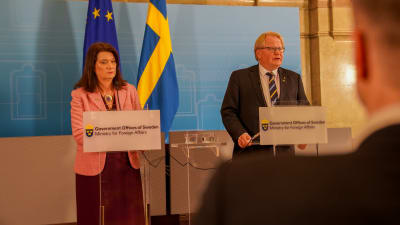 Utrikesminister Ann Linde och försvarsminister Peter Hultqvist står framför Sveriges flagga.