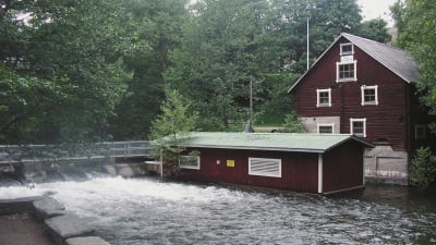 Två röda byggnader intill forsande vatten.