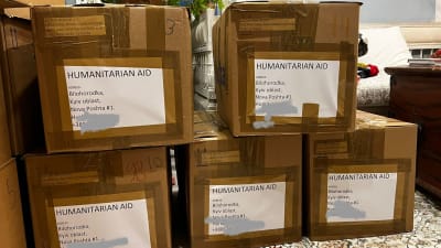 Stora bruna papplådor med texten Humanitarian aid och adress till Ukraina. Lådorna är radade på varann i ett vanligt vardagsrum.