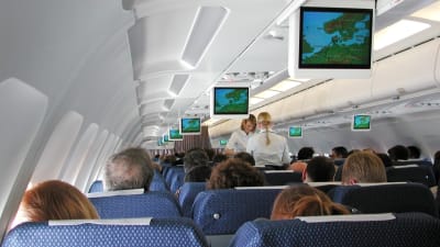Passagerare och två flygvärdinnor inne i ett flygplan.