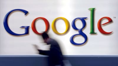 Man med mobil passerar en stor Google-logotyp. 