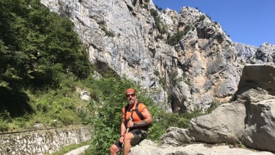 Björn Roos sitter på en sten i ettt bergit landskap.