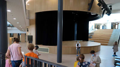 Bild av en stor rund scen som finns i mitten av det nya Laurentiushuset. Kring scenen finns männsikro som är på rundvadring i byggnaden. 