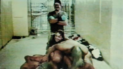 Amerikanska soldater poserar bakom nakna irakiska fångar som tvingats sitta på varandra.