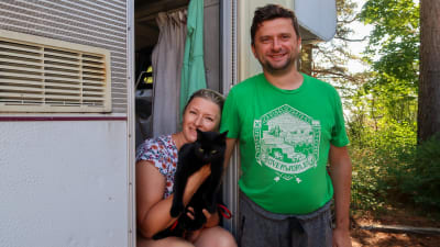 Porträtt av Irina och Vladimir Rogojin som står i dörren till deras husbil. Irina har en katt i famnen.