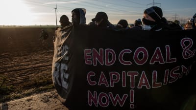 Andreas Malm och en grupp andra människor ute på en klimataktion. Gruppen har masker framför ansiktet och står invirade i en banderoll med budskapet "End coal & capitalism now!"