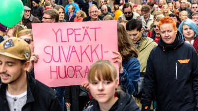 Demonstranter med en skylt med texten "Ylpeät suvakkihuorat".