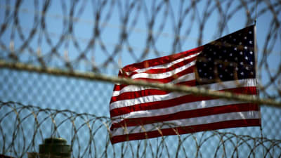 En amerikansk flagga bakom taggtråd som omger fånglägret Guantanamo Bay