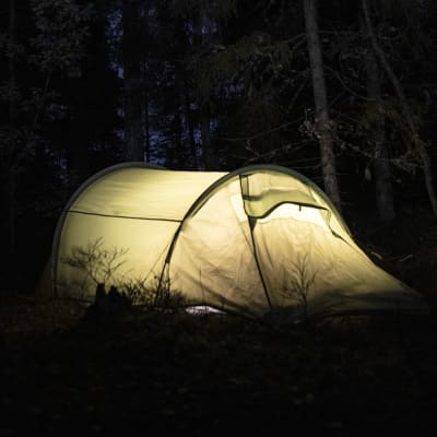 Valaistu teltta pimeässä metsässä.