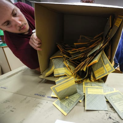 Vaalivirkailija kaataa äänestyslippuja ulos laatikosta.
