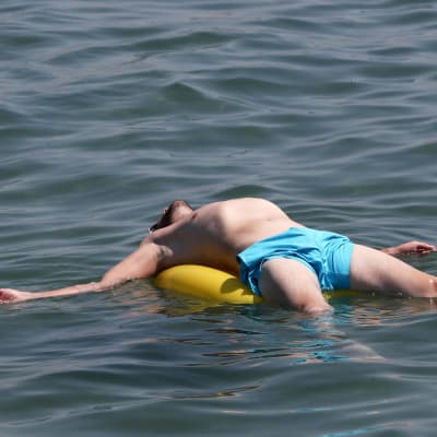 Henkilö makaa uimarenkaan päällä vedessä.