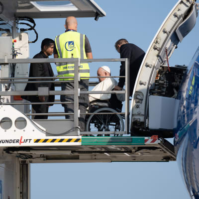Påve Franciskus i rullstol lyfts ombord på ett flygplan med hjälp av en stor lyft.