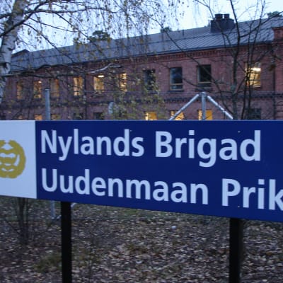 En skylt där det står Nylands Brigad, i bakgrunden en tegelbyggnade på Dragsviksområdet i Ekenäs.