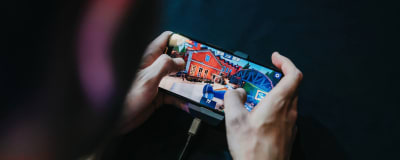 En man spelar ett mobilspel. På skärmen syns en röd byggnad.