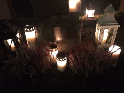 Bild på en grav med gravljus i kvällsmörker.