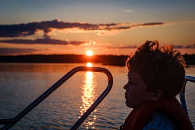 Pojke i motorbåt med solnedgång i bakgrunden.